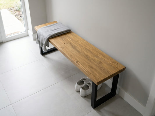 Wooden bench with a towel draped over it in a room with white tiled floor and walls.