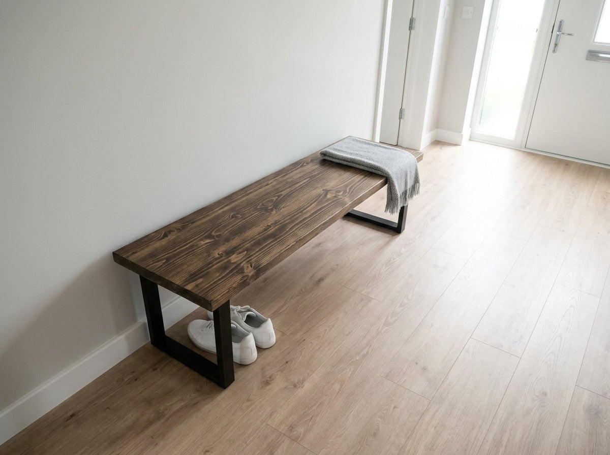 Wooden bench with a towel draped over it in a room with wooden flooring and a white wall.