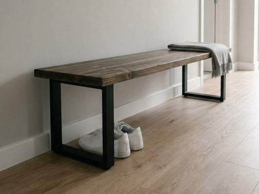Wooden bench with black legs in a minimalistic room with light wood flooring and white walls.